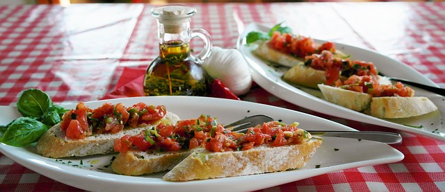 fresh bruschetta pieces on white plate, oil and garlic bulb in background